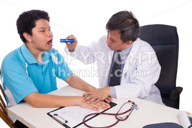 Asian doctor inspecting throat of patient in clinic - ThamKC Royalty-Free Photos