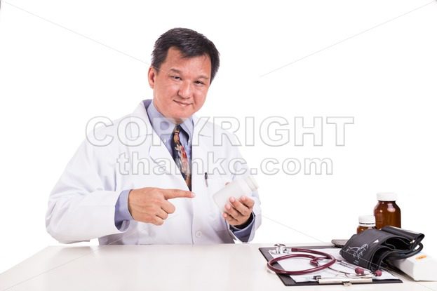 Matured Asian medical practitioner pointing on medicine bottle - ThamKC Royalty-Free Photos