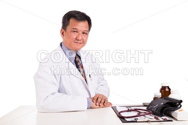 Matured Asian medical practitioner seated behind desk - ThamKC Royalty-Free Photos