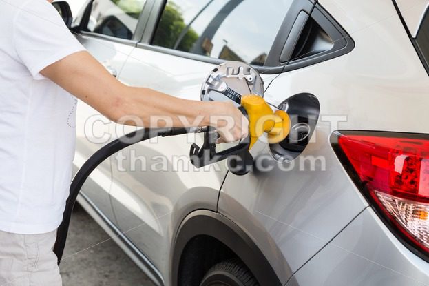 Person holding yellow nozzle filling petrol into car - ThamKC Royalty-Free Photos