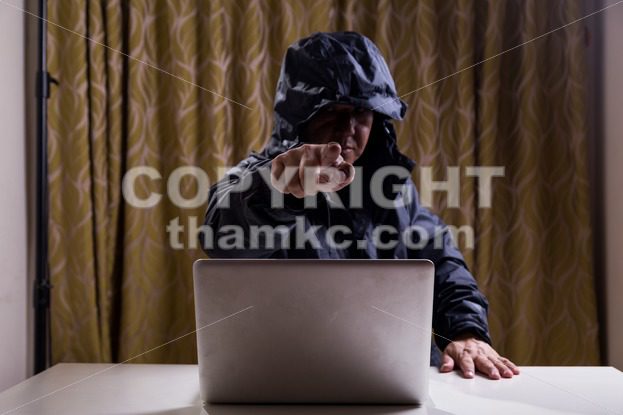 Angry Asian hacker pointing finger to audience while hacking network - ThamKC Royalty-Free Photos