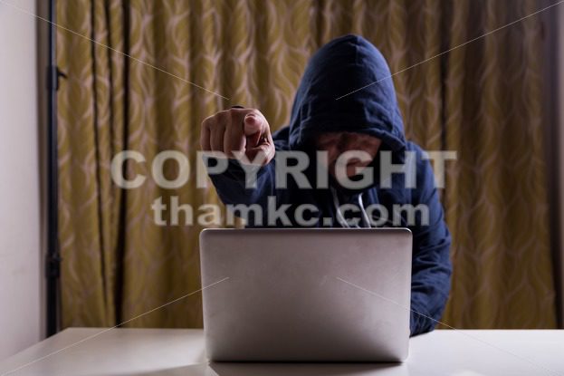Angry Asian hacker pointing finger to camera while hacking network - ThamKC Royalty-Free Photos