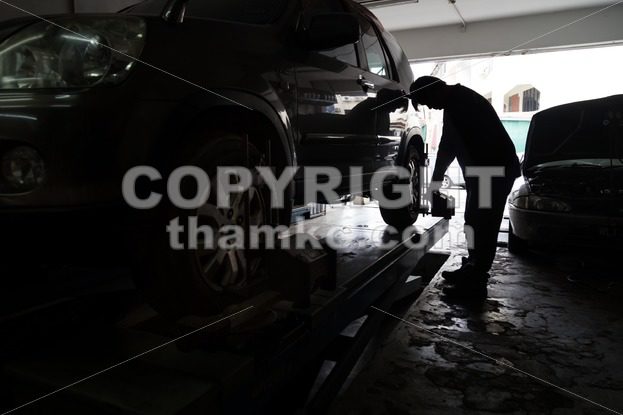 Silhouette of mechanic fixing car aligner onto car wheel - ThamKC Royalty-Free Photos