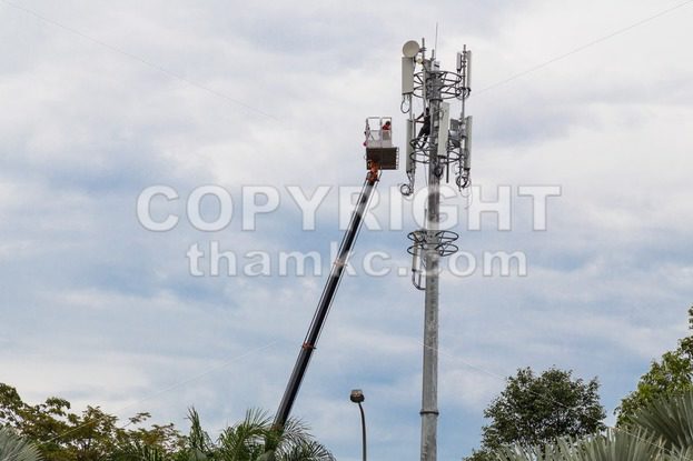 Two workers on crane installing mobile network communication antenna - ThamKC Royalty-Free Photos