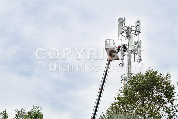 Two workers on crane installing mobile network communication antenna - ThamKC Royalty-Free Photos