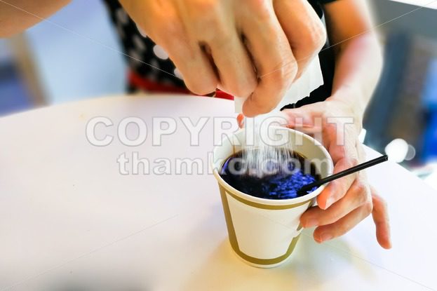 Women pouring sugar granules from sachet into black coffee - ThamKC Royalty-Free Photos
