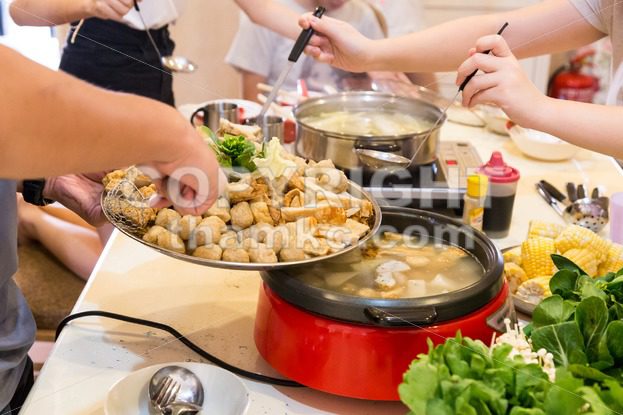 Hand adding ingredient into Asian steamboat pot meal - ThamKC Royalty-Free Photos