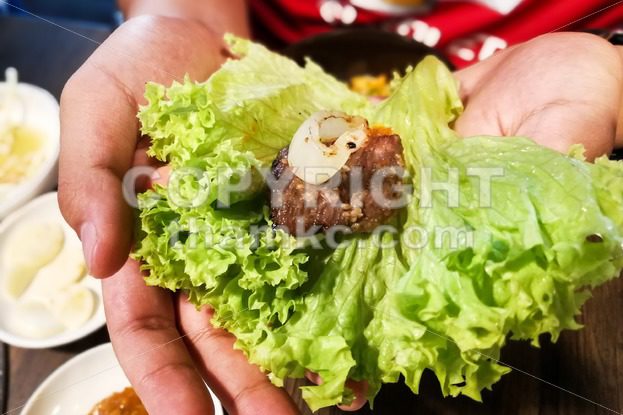 Hand holding korean barbecue beef and garlic wrap with salad - ThamKC Royalty-Free Photos