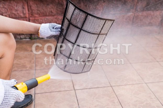 Person spraying water onto air conditioner filter to clean dust - ThamKC Royalty-Free Photos