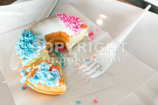 Unfinished donut glazed with sugar coating and sprinkles on plate - ThamKC Royalty-Free Photos