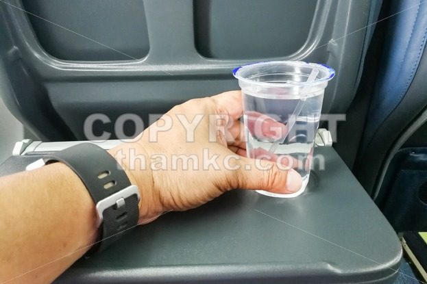 Hand holding disposable mineral water on table in air plane - ThamKC Royalty-Free Photos
