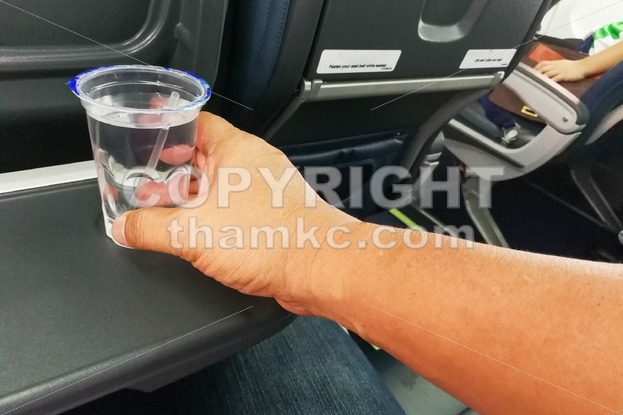 Hand holding disposable mineral water on table in air plane - ThamKC Royalty-Free Photos