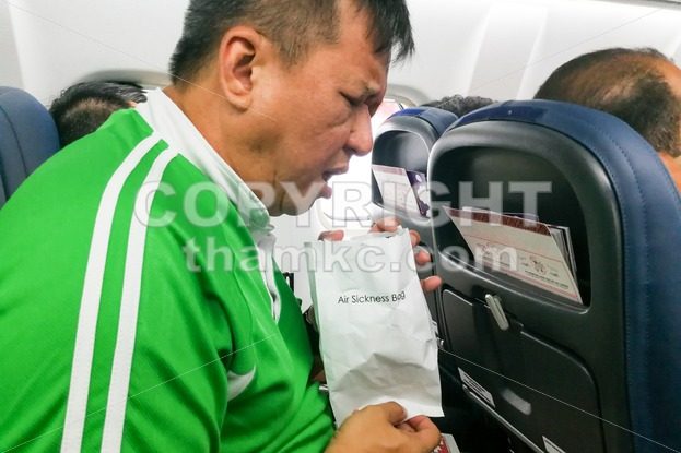 Nauseous air sickness Asian man vomiting into air sickness bag - ThamKC Royalty-Free Photos