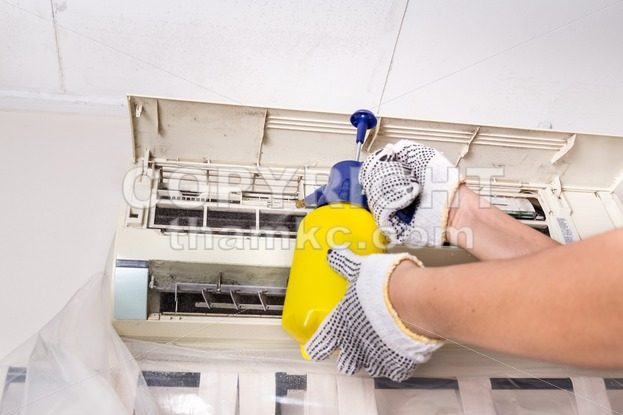 Technician spraying chemical water onto air conditioner grid to clean - ThamKC Royalty-Free Photos